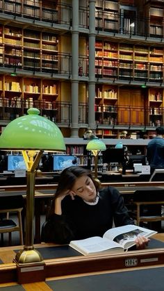 a woman sitting at a table in a library reading a book and talking on the phone