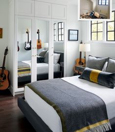 a bed room with a neatly made bed and two guitars hanging on the closet doors