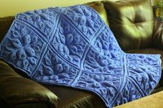 a blue blanket sitting on top of a couch next to a brown leather sofa cushion