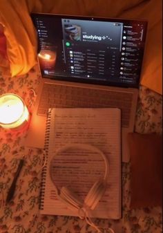 an open laptop computer sitting on top of a bed next to a book and headphones