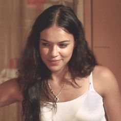 a woman with long dark hair wearing a white tank top and holding a cell phone in her hand