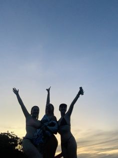 three women in bathing suits standing on the beach with their arms up and hands raised