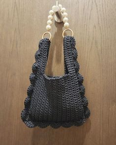 a crocheted purse hanging from a hook on a wooden table next to beads