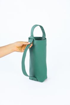 a hand is holding a green bag on a white background with the handle extended to it