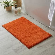 an orange bath mat sitting on top of a bathroom floor next to a white tub