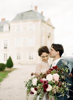 a bride and groom are standing in front of a large building with flowers on it