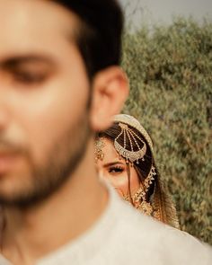 a man and woman standing next to each other in front of some olive trees with an umbrella on their head