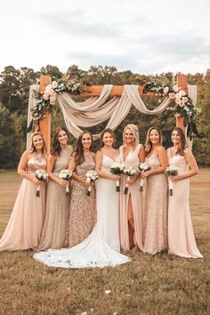 a group of women standing next to each other in front of a wooden arch with flowers