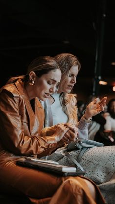 two women sitting next to each other looking at something on their cell phone and tablet