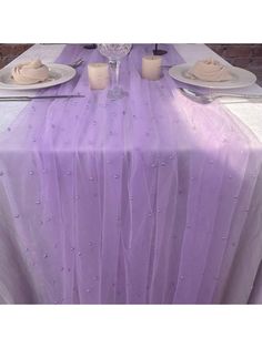 the table is covered with purple tulle and place settings for two people to sit at