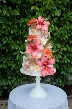 a white cake with pink and orange flowers on it sitting on top of a table