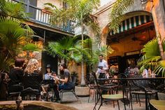 people are sitting at tables in an outdoor cafe with palm trees and potted plants