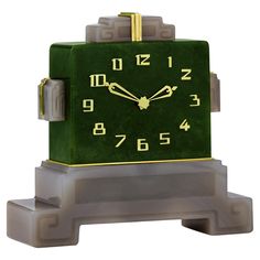 a green and gold clock sitting on top of a gray block with two hands in the middle