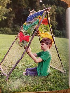 a young boy sitting in the grass with a colorful piece of art hanging from it's sides