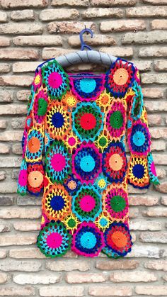 a colorful crocheted sweater hanging on a brick wall