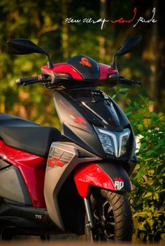 a red and gray scooter parked in front of some bushes with trees behind it