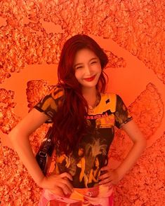 a woman standing in front of an orange wall with her hands on her hips and smiling at the camera