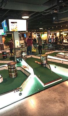 several people are playing miniature golf at the indoor game room with many tables and stools