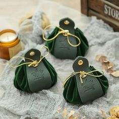 three small green bags with gold handles sitting on a lace covered table cloth next to a candle