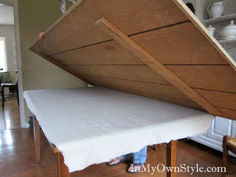 a person standing next to a table with a mattress on it's bottom shelf