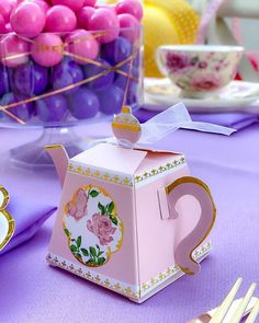 a pink teapot shaped like a tea pot on top of a purple table cloth