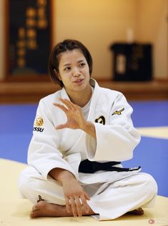 a woman sitting on top of a blue mat in a karate uniform holding her hand out