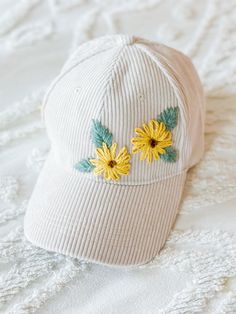 a white hat with yellow flowers on the front and green leaves on the side sitting on a bed