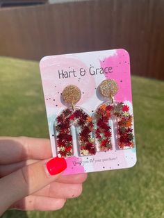 a person holding up two pairs of red and white earrings with glitter accents on them