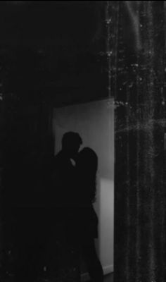 black and white photograph of two people kissing in front of a window with curtains behind them