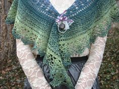 a woman wearing a green and blue shawl with lace on the top, holding her hands in her pockets