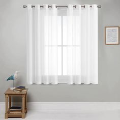 a white window curtain hanging on the side of a wall next to a small table