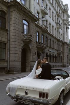 a bride and groom are sitting in the back of a convertible car on a city street