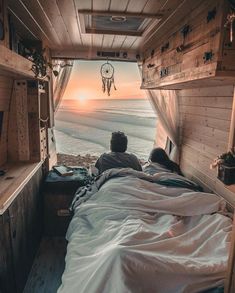 a person laying in bed looking out at the ocean from inside a truck with its door open