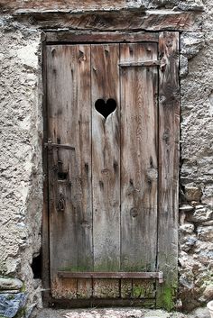 an old wooden door with a heart shaped hole in the middle, on a stone wall