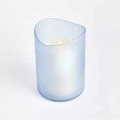 a white candle is sitting in a glass vase on a table with a white background