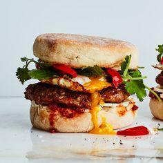 two burgers with meat, cheese and vegetables on them sitting next to each other