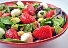 a salad with strawberries and spinach in a red bowl on a white table