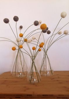 three clear vases with flowers in them on a wooden table next to a white wall