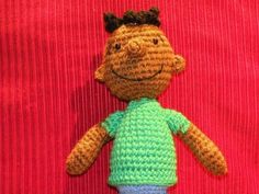 a crocheted stuffed animal with a green shirt and blue pants on a red background