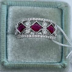 a diamond and ruby ring sits in a velvet box with white thread on the edge