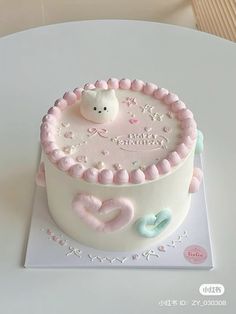 a white cake with pink frosting and decorations on it's side sitting on a table