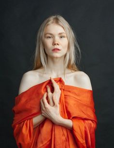 a woman in an orange dress with her hands folded over her chest and looking off to the side