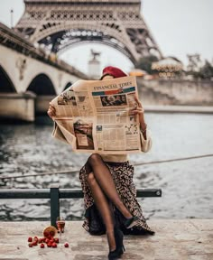 a woman sitting on a bench in front of the eiffel tower reading a newspaper