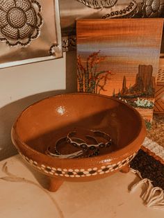 a brown bowl sitting on top of a counter next to pictures and other art work