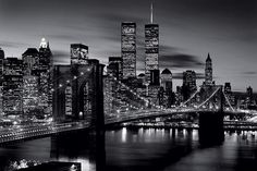 a black and white photo of the brooklyn bridge at night, with skyscrapers in the background