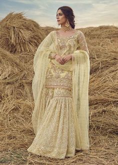 a woman standing in front of hay bales wearing a white dress and shawl