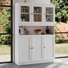 a white cabinet filled with lots of bottles and glasses next to a large glass window