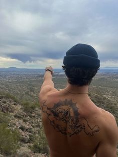 a man with a tattoo on his back pointing at the sky and clouds in the distance