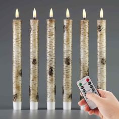 a person is holding a remote control in front of five lit candles that are lined up