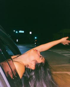 a woman leaning out the window of a car with her arm outstretched in the air